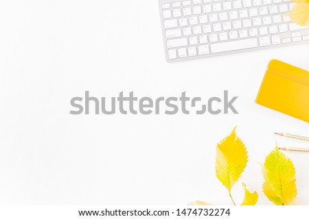 Flat lay blogger or freelancer workspace with a notebook, keyboard, colorful autumn leaves on a white background