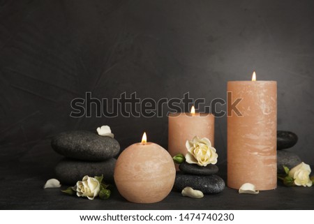 Burning candles, spa stones and flowers on dark grey table, space for text