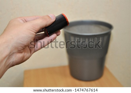 A man's hand holds a battery and is about to throw it in an urn. Disposal of environmentally hazardous waste.