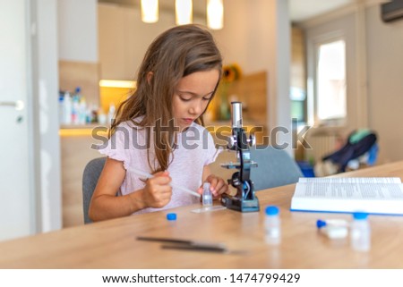 Portrait of Curious Little Scientist. Beautiful elementary schoolgirl uses a microscope for science project. Little girl concentrates while using microscope. Back to school concept.