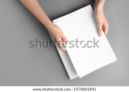 Woman holding blank paper sheets for brochure at grey table, top view. Mock up