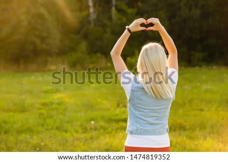 A young girl making heart symbol with her hands at sunset