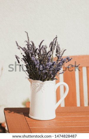 Freshly picked lavender in white jug on wooden table in garden with white wall