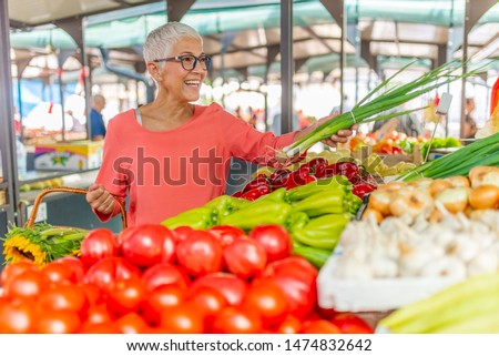 Senior woman on the market. Mature Female Customer Shopping At Farmers Market Stall.  Woman shopping at the local Farmers market. Beautiful senior woman buying vegetables. Royalty-Free Stock Photo #1474832642