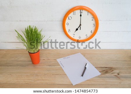 Round clock on a white wall, green houseplant and a blank sheet of paper with a pen. Business planning