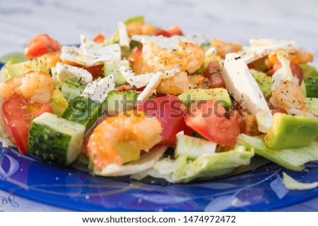 Healthy organic food concept. Large glass plate with Greek salad. Tomatoes, cucumbers, avocado, feta cheese, shrimp, salad and spices doused with olive oil. Selective focus. Side view