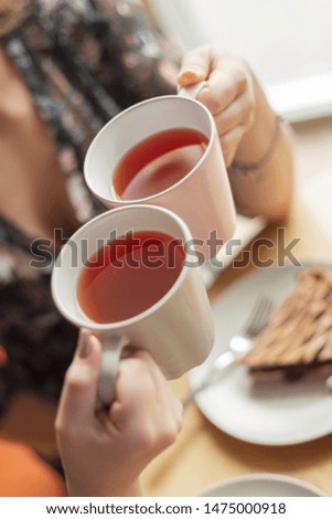 the process of drinking tea by girlfriends in a cafe. Photo of hands holding mugs with red fruit tea