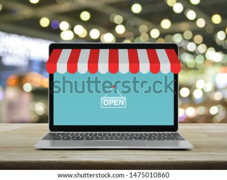 Modern laptop computer with online shopping store graphic and open sign on wooden table over blur light and shadow of shopping mall, Business internet shop online concept