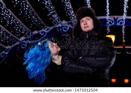 Portrait of couple on the city rink in a winter evening. Guy and girl with blue hair in a dark night and twinkles lighting above them