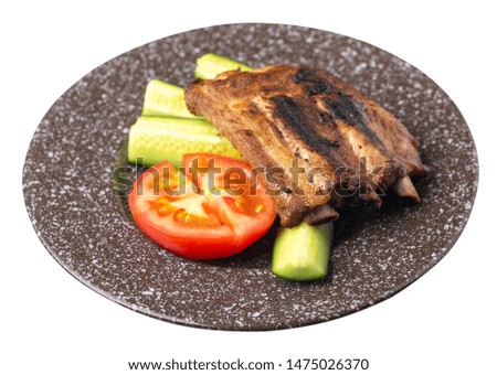 grilled pork ribs with sliced cucumbers and tomatoes on a brown with a marble crumb plate. pork ribs isolated on white background. ribs grill top side view
