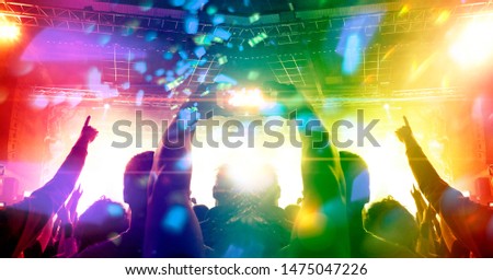 Concert shot of a colourful arena with festive clapping people in front of a large stage