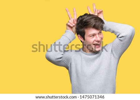 Young handsome man wearing winter sweater over isolated background Posing funny and crazy with fingers on head as bunny ears, smiling cheerful