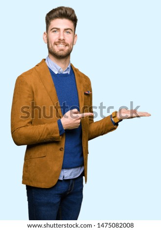 Young handsome business man amazed and smiling to the camera while presenting with hand and pointing with finger.