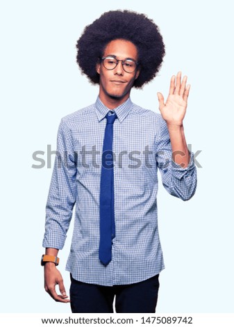 Young african american business man with afro hair wearing glasses Waiving saying hello happy and smiling, friendly welcome gesture