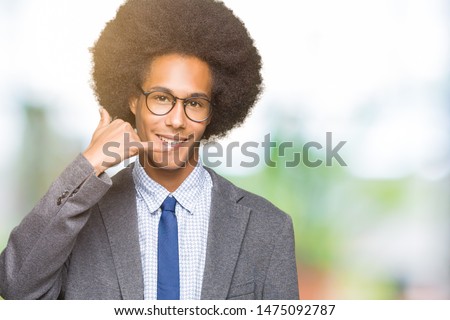 Young african american business man with afro hair wearing glasses smiling doing phone gesture with hand and fingers like talking on the telephone. Communicating concepts.