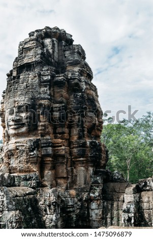 A sculpture carved from a rustic rock in the form of faces on four of its parts on the roofs of the ruins of the Bayon temple in Ankgor Thom, Cambodia - UNESCO World Heritage Site 1992- Vertical image