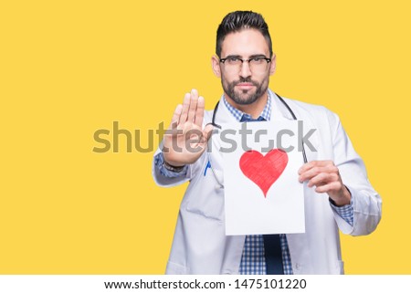 Handsome young doctor man holding paper with red heart over isolated background with open hand doing stop sign with serious and confident expression, defense gesture