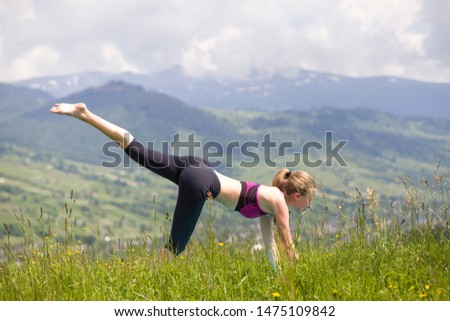 Attractive slim young woman doing yoga exercises outdoors on copy space background of mountains.