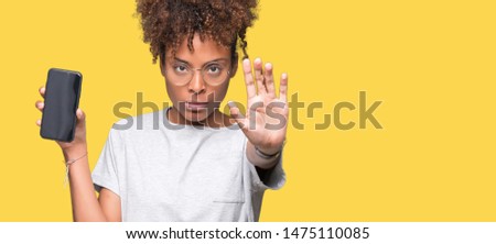 Young african american woman showing smartphone screen over isolated background with open hand doing stop sign with serious and confident expression, defense gesture
