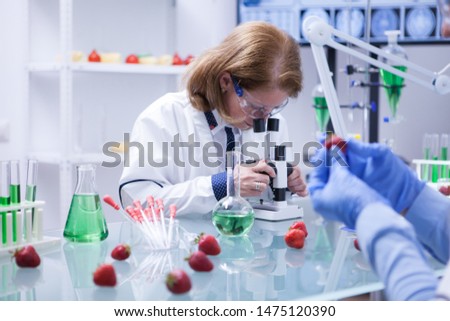 Mdiddle age female scientist with protection glasses looking into her microscope. Research lab.