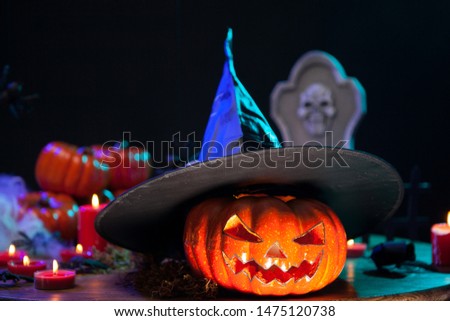 Orange scary pumpking for halloween wearing a black witch hat. Halloween decoration on wooden table.