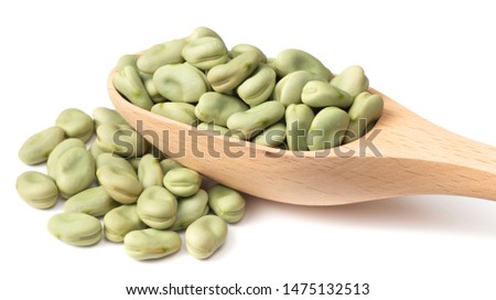 uncooked dried green faba beans in the wooden spoon, isolated on white background