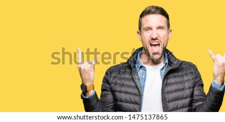 Handsome man wearing winter coat shouting with crazy expression doing rock symbol with hands up. Music star. Heavy concept.