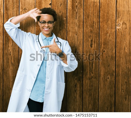 Young african american doctor woman wearing medical coat over isolated background smiling making frame with hands and fingers with happy face. Creativity and photography concept.
