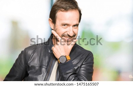 Middle age handsome man wearing black leather jacket looking confident at the camera with smile with crossed arms and hand raised on chin. Thinking positive.