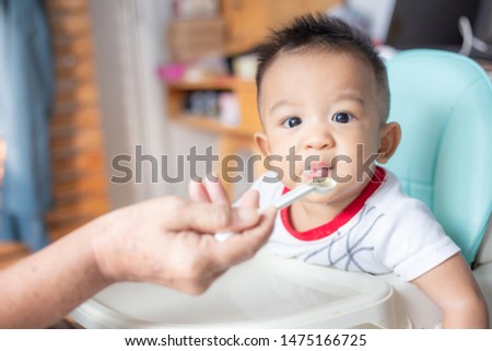 Asian infant baby child boy sitting on baby chair try to eating blend food in home
