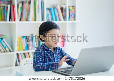 Picture of little boy using a laptop computer while sitting in the library with bookshelf background