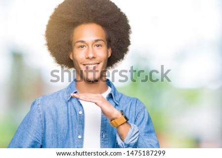 Young african american man with afro hair gesturing with hands showing big and large size sign, measure symbol. Smiling looking at the camera. Measuring concept.