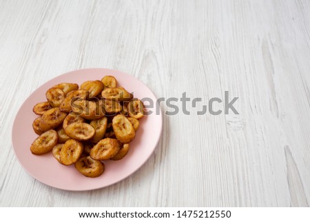 Homemade fried plantains on a pink plate on a white wooden surface, low angle view. Copy space.