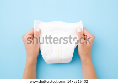 Woman hands holding white baby diaper on pastel blue background. Closeup.
