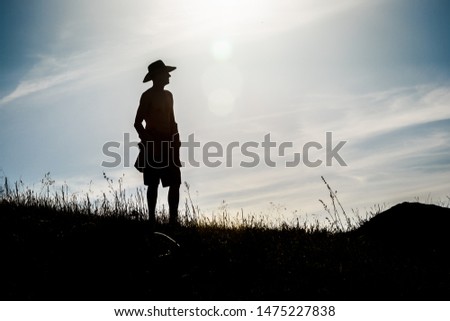 Silhouette of man in hat staying on hill