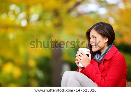 Autumn / fall woman drinking coffee looking at forest foliage copy space thinking. Happy smiling multi-ethnic Asian Chinese / Caucasian female model in red coat enjoying hot drink outdoor.
