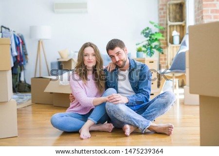 Young beautiful couple moving to a new house sitting on the floor with serious expression on face. Simple and natural looking at the camera.