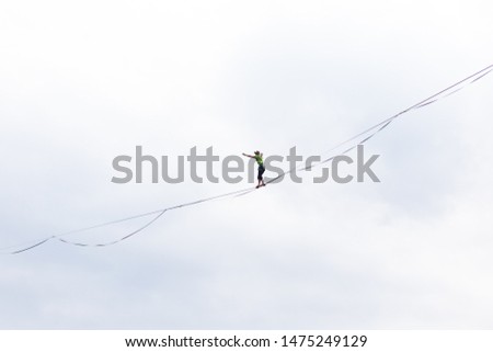 Highline on the background of the cloudy sky. A man is walking along a stretched sling. Performance of a tightrope walker on a background of clouds. Man balances over the abyss. A decisive step.