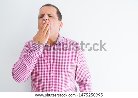 Middle age man wearing business shirt over white wall bored yawning tired covering mouth with hand. Restless and sleepiness.