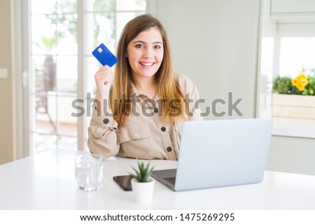 Beautiful young woman shopping online using laptop and credit card with a happy face standing and smiling with a confident smile showing teeth