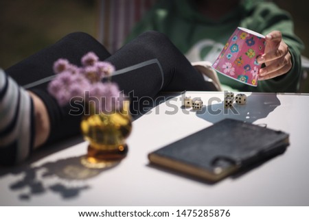 cozy, quiet scene at the table. Dice fall out of the dice cup. Selective sharpness. Writing pad and flowers are on a table. Legs on the table