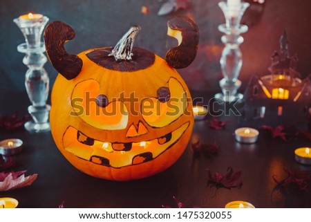 Close up carved luminous pumpkin with scary evil face, burning candles and paper silhouettes of bats, castle, ghosts on black stone background. Spooky holiday symbols and celebration concept