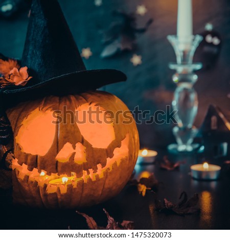 Close up carved pumpkin in witch hat, burning candles and paper silhouettes of bats, castle, ghosts on black stone background. Head jack lantern with scary evil faces. Spooky holiday concept. Square