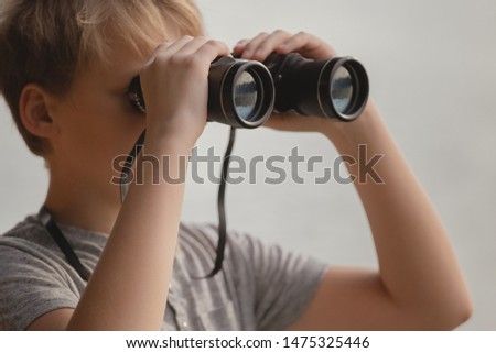 Closeup portrait of handsome blond white kid holding old vintage black binocular in hands and looking at something interesting. Horizontal color photography.