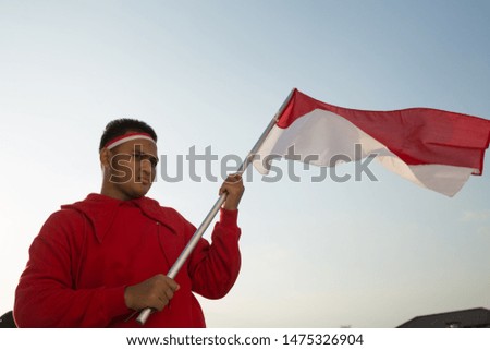 Portrait of asian man holding a Indonesian red and white  flag under a bright blue sky