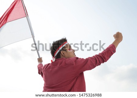 Portrait of asian man holding a Indonesian red and white  flag under a bright blue sky