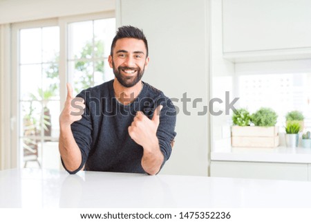 Handsome hispanic man wearing casual sweater at home success sign doing positive gesture with hand, thumbs up smiling and happy. Looking at the camera with cheerful expression, winner gesture.