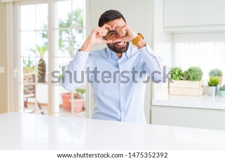 Handsome hispanic business man Doing heart shape with hand and fingers smiling looking through sign