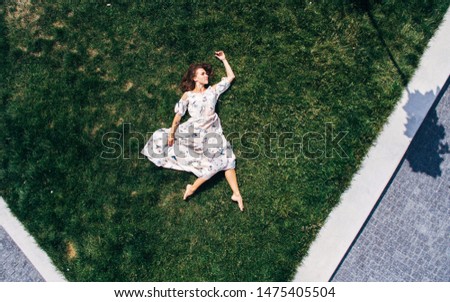 Surrealism. The girl lies on a green lawn in a dress. Aerial view