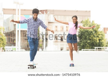 Cheerful african american teenagers racing on modern skateboards against cityscape. Copy space